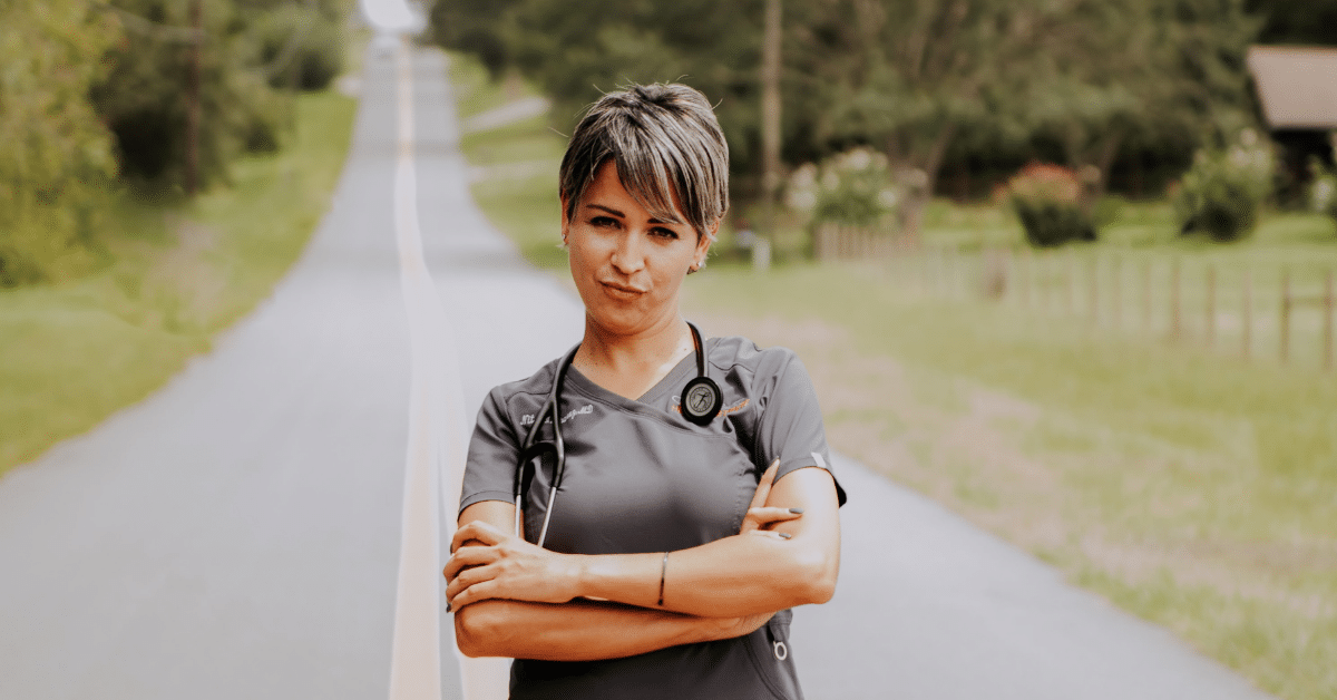 Dr. Nitza Alvarez stands on a road in scrubs with her arms crossed confidently as an advocate for women’s health